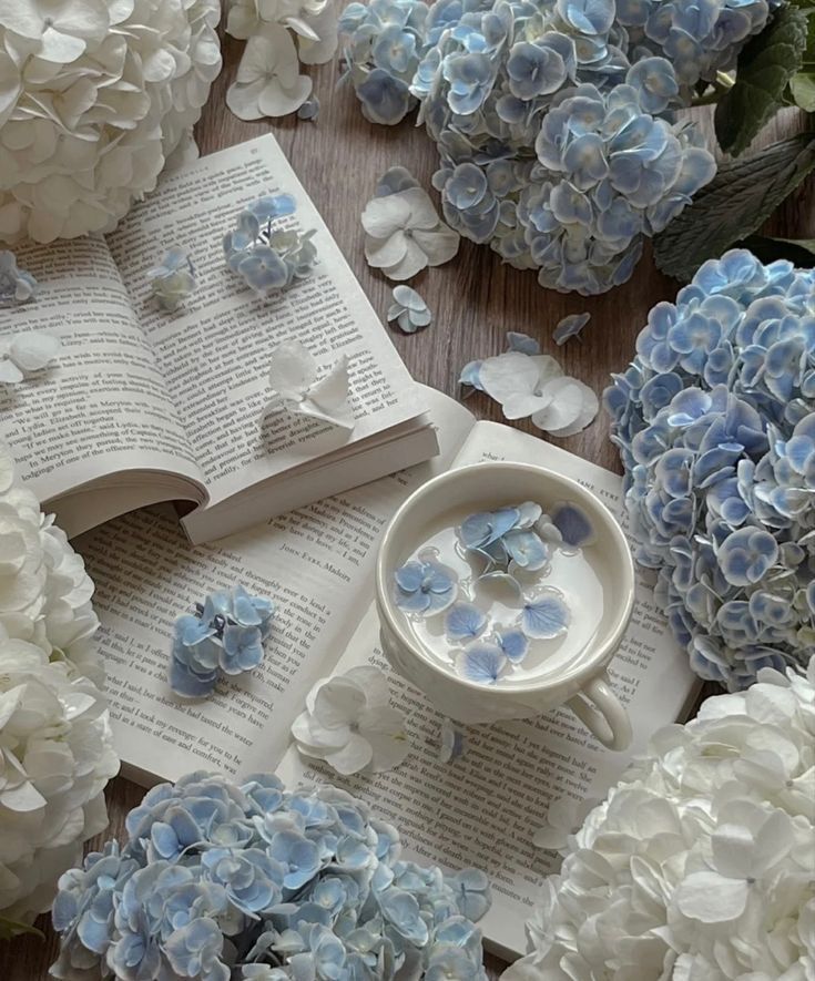 blue and white flowers are scattered around an open book