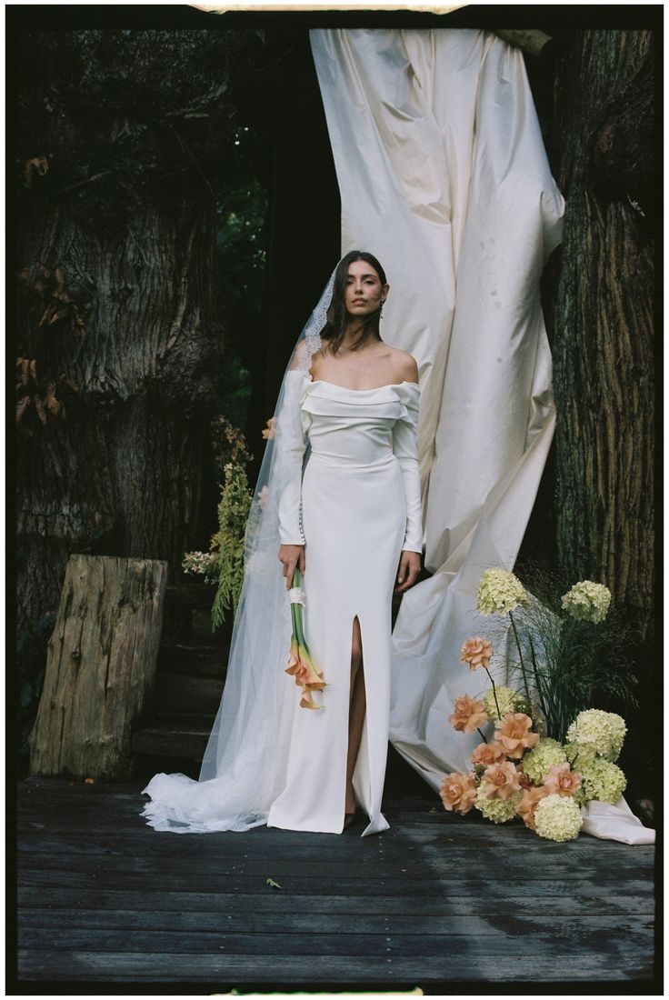 a woman in a white wedding dress standing next to a tree with flowers on it