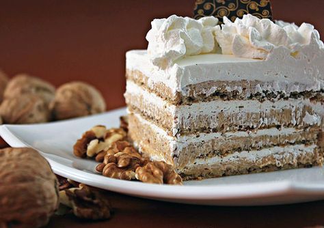 a piece of cake with white frosting and nuts on a plate next to it