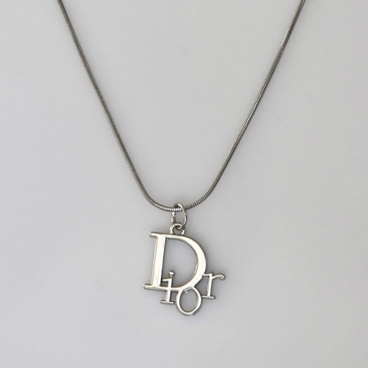 Authentic Christian Dior logo pendant set on a stainless steel 18 inch chain. Luxury Silver Jewelry With Silver-tone Logo, Affordable Classic Silver Charm Necklaces, Christian Dior Jewelry Vintage, Saint Laurent Necklace Silver, Silver Metal Snake Chain Charm Necklace, Silver Charm Necklaces With Snake Chain, Vintage Silver Necklace With Logo Charm, Silver Charm Necklace With Logo As Gift, Luxury Silver Charm Necklace With Round Pendant