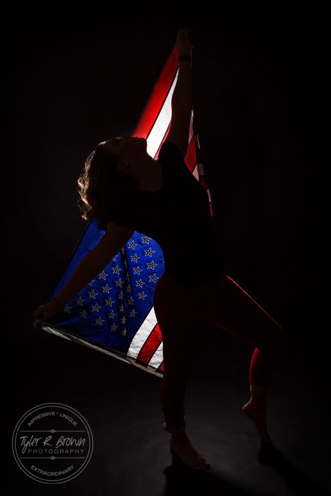 a woman is holding an american flag in the dark with her arms stretched out and legs crossed