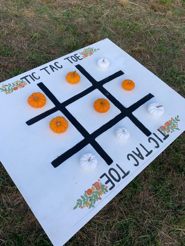 a tic - tac - toe board sitting in the grass with pumpkins on it