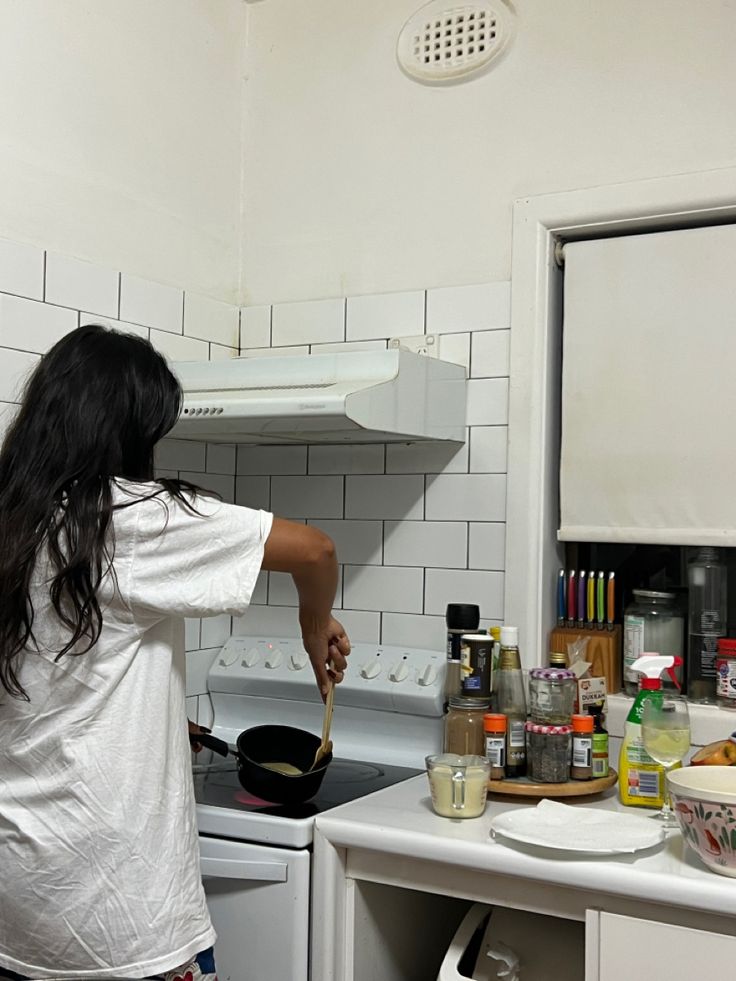 a woman cooking in a kitchen with white tile walls