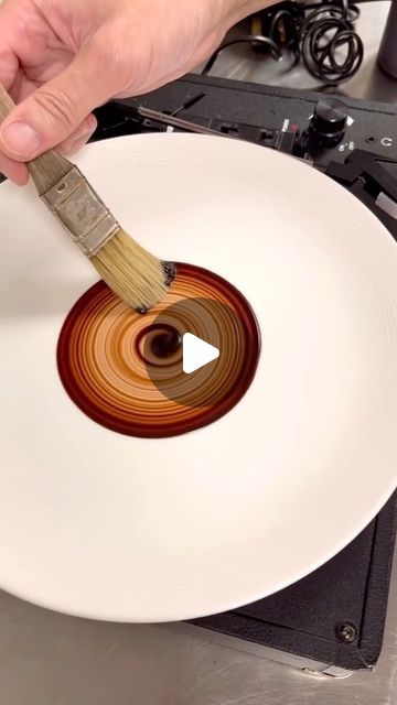 a person is using a brush to paint a white plate with brown swirl on it