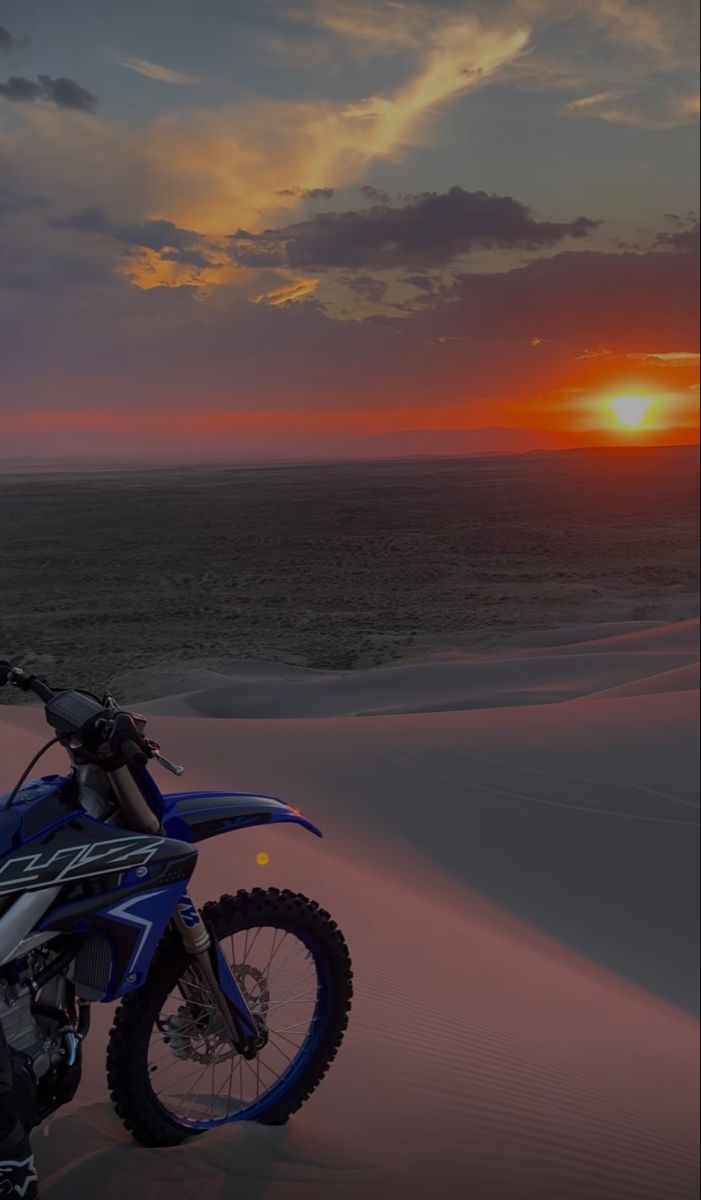 a dirt bike parked in the sand at sunset