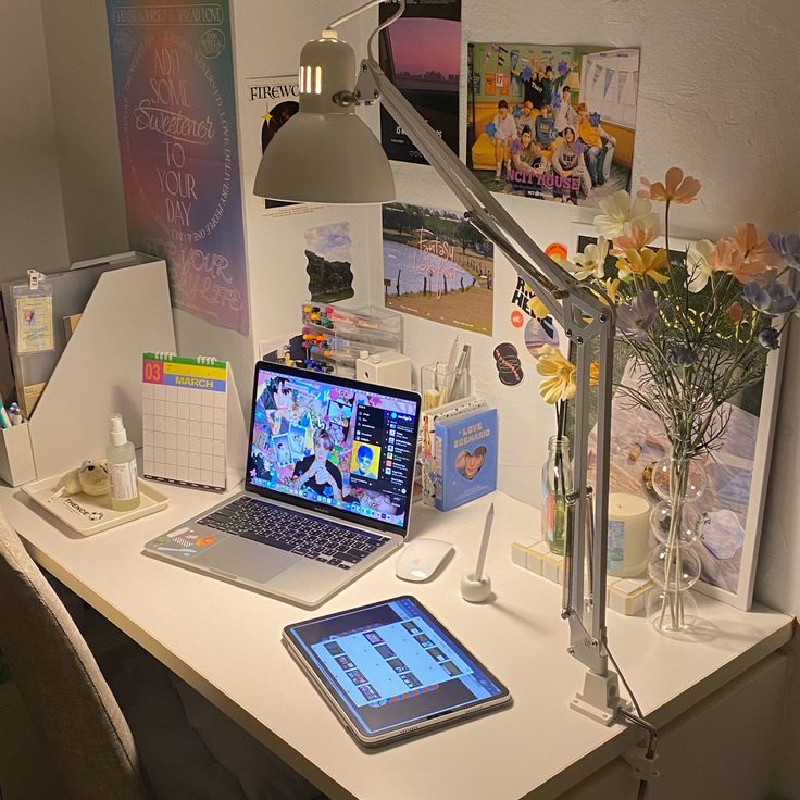 a laptop computer sitting on top of a white desk next to a lamp and flowers