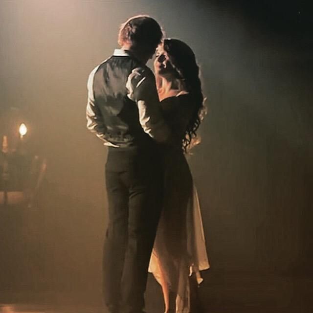 a man and woman dancing on stage in front of a spotlight light with their arms around each other