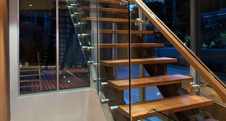 a stair case with glass railing and wooden handrails in a house at night