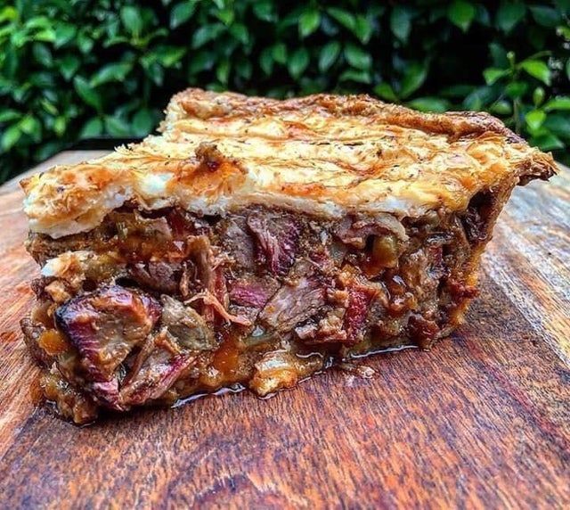 a piece of meat pie sitting on top of a wooden table next to some bushes