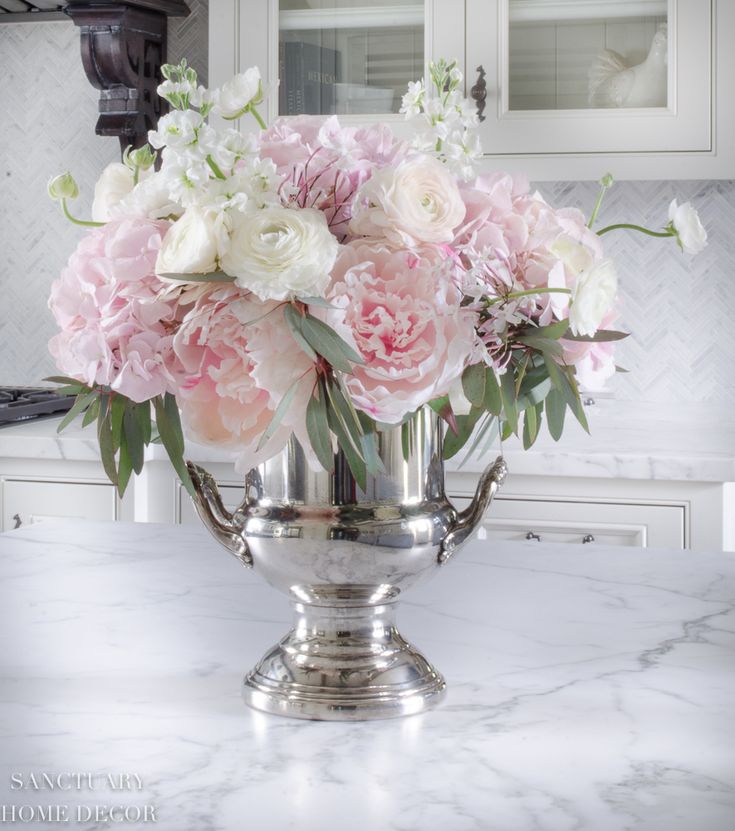 a silver vase filled with pink and white flowers on top of a marble countertop