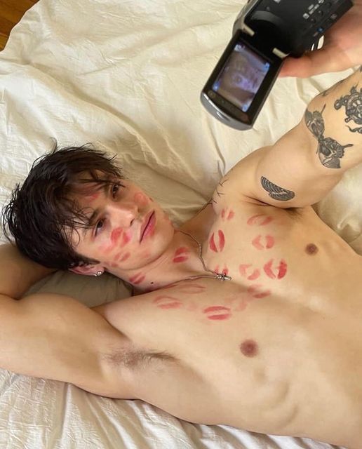 a shirtless man laying in bed with red spots on his body and cell phone