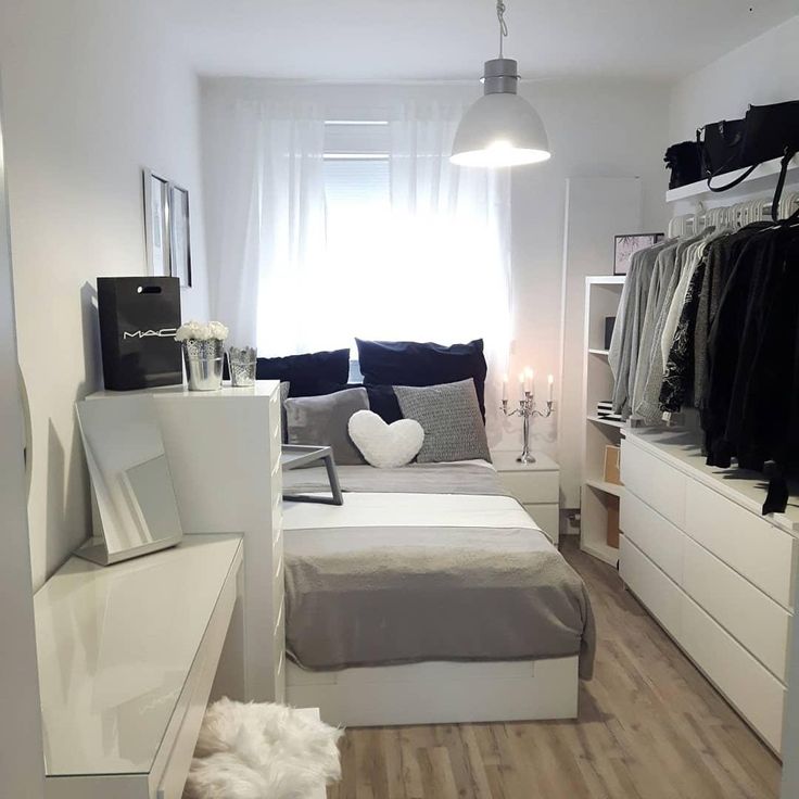 a bedroom with white walls and wood flooring has a bed, dressers, and shelves