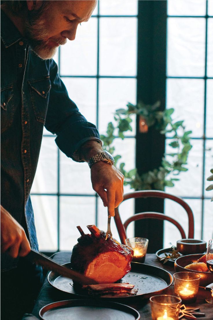 a man cutting up a piece of meat on top of a plate next to candles