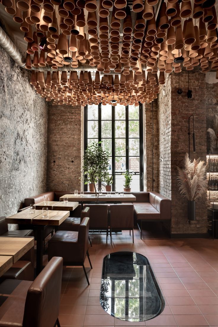 a restaurant with lots of tables and chairs in front of a large window that has potted plants hanging from the ceiling