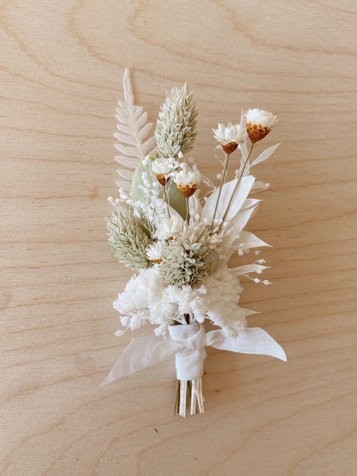 a bouquet of white flowers and greenery on a wooden surface with woodgrain