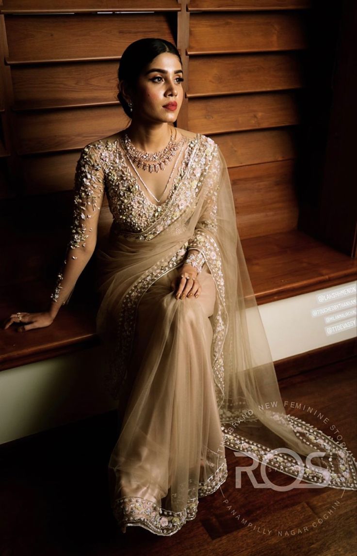 a woman sitting on top of a wooden bench wearing a beige sari and jewelry