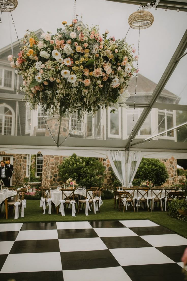 an outdoor reception setup with flowers hanging from the ceiling and checkerboard flooring