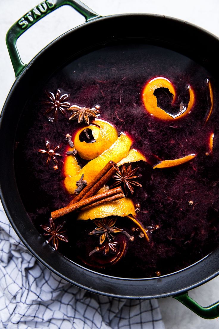 a pot filled with purple liquid and orange peels on top of a white table cloth