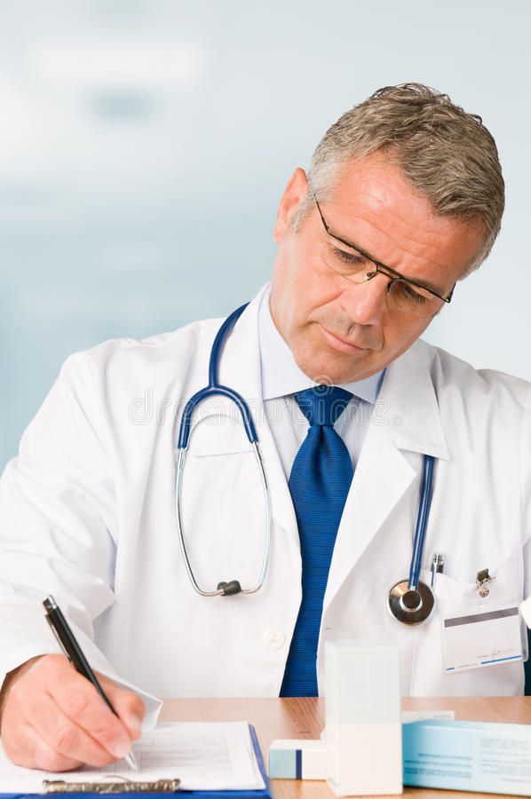 a man in a white lab coat writing on a piece of paper with a stethoscope next to him