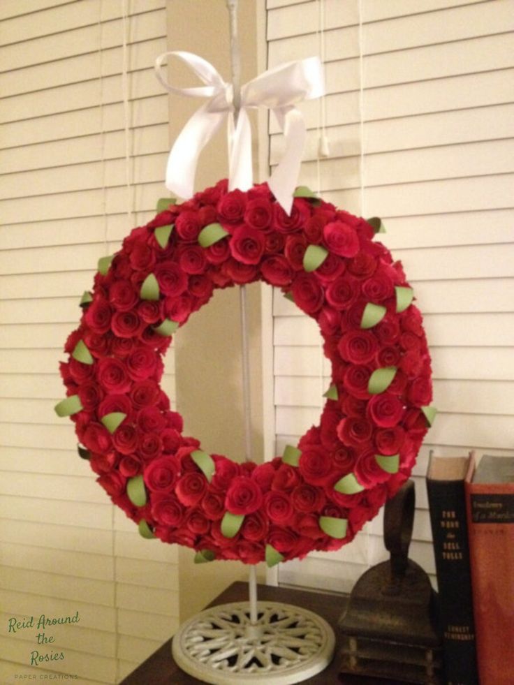 a red rose wreath on top of a wooden table next to a book and lamp