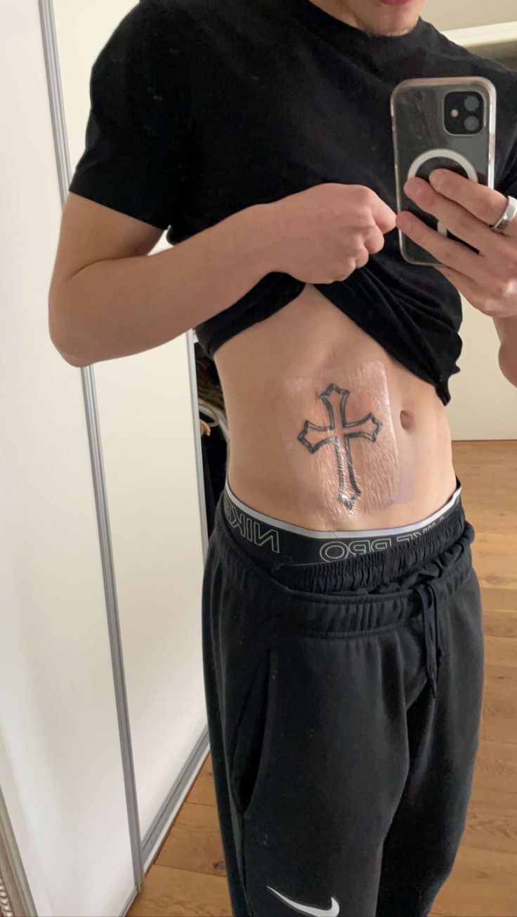 a man with a cross tattoo on his stomach holding a cell phone and taking a selfie