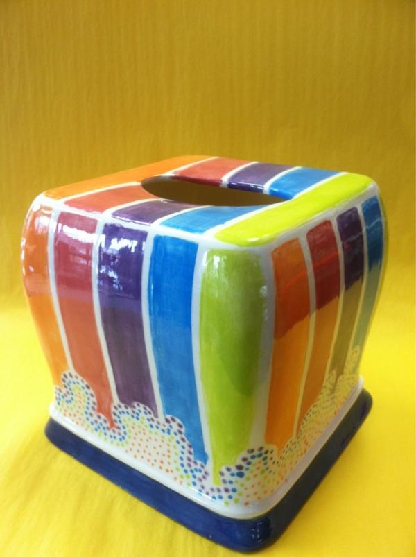 a multicolored ceramic tissue dispenser sitting on a yellow tablecloth