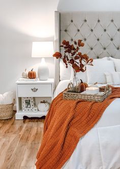 a bed with white sheets and orange blankets on it, next to a night stand