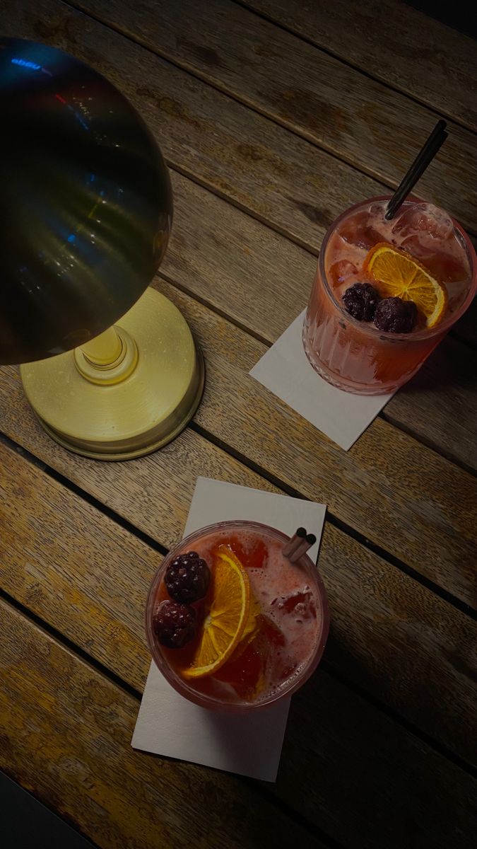 two glasses filled with drinks sitting on top of a wooden table