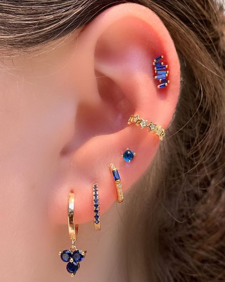 a woman wearing ear piercings with blue and gold colored stones on the side of her ear