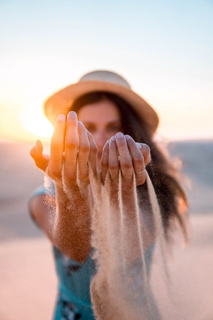 a woman in a hat is throwing sand into the air with her hands and fingers