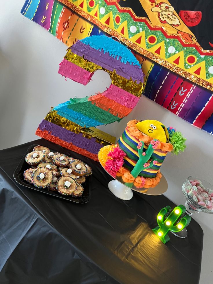 a table topped with a number two cake next to cupcakes and other treats