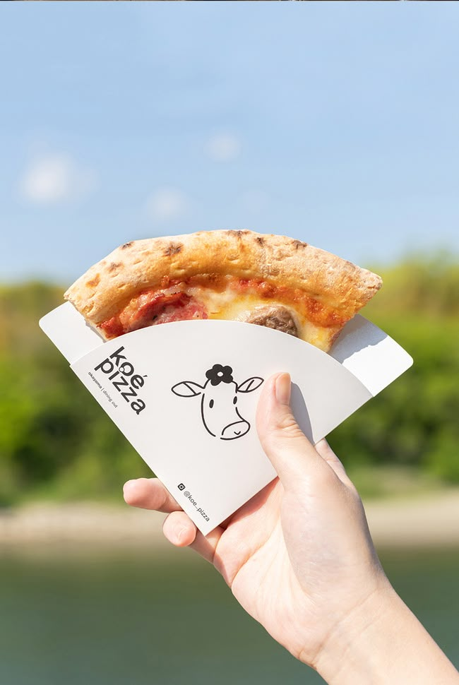 a hand holding up a piece of pizza with a cow on it's face