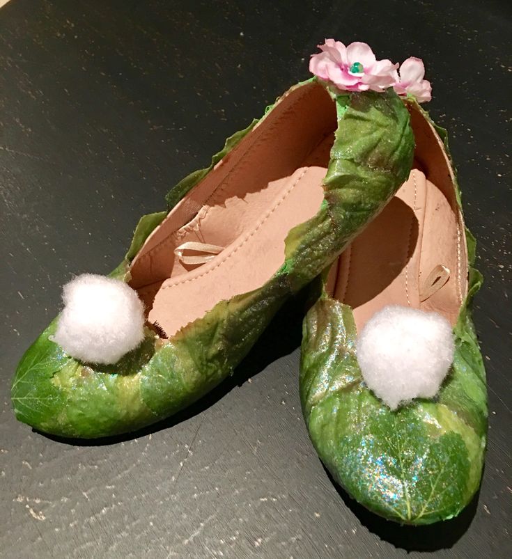 two green shoes with white pom - poms on them sitting on a table