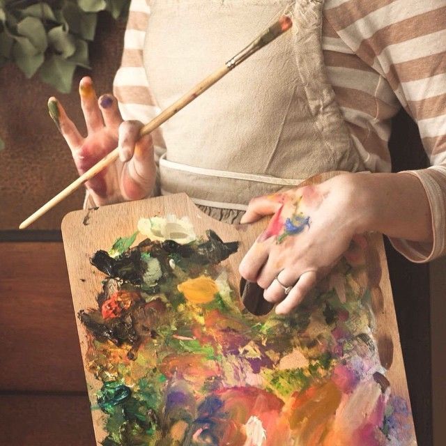 a woman is holding a paintbrush and painting on a wooden board with multiple colors