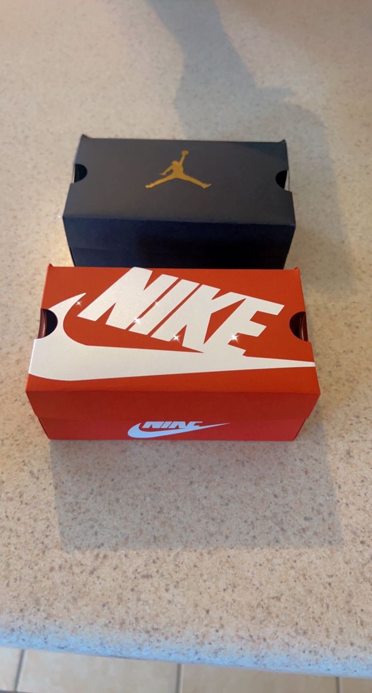 two nike boxes sitting on top of a counter next to each other, one red and one black