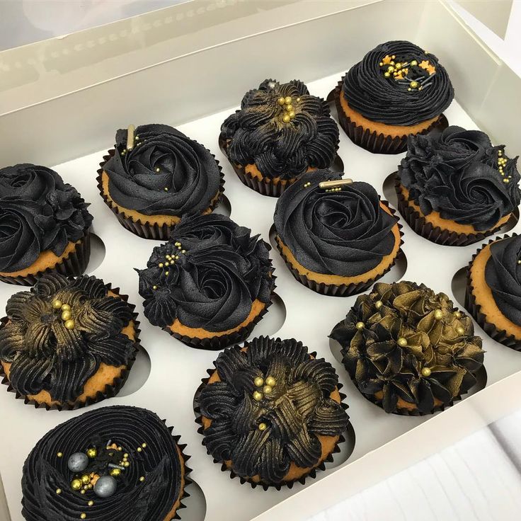 twelve decorated cupcakes in a white box with gold decorations on the top and sides