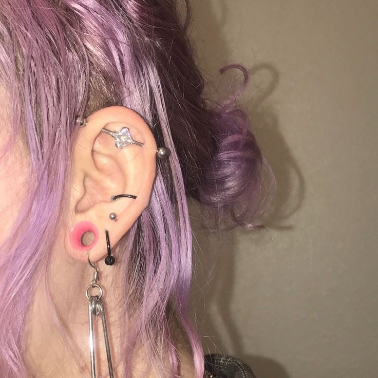 a woman with pink hair has ear piercings on her ears