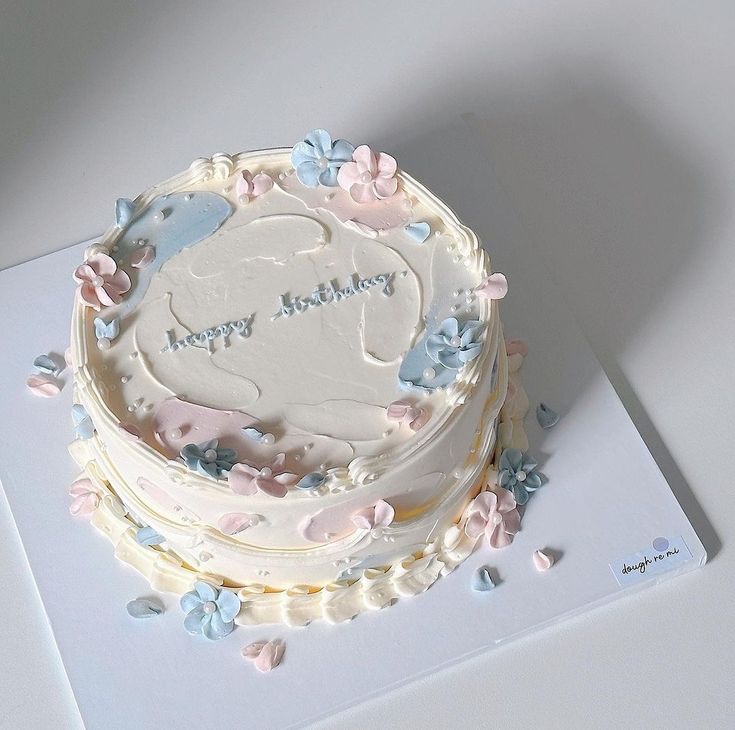 a birthday cake with white frosting and blue flowers on the top is sitting on a card