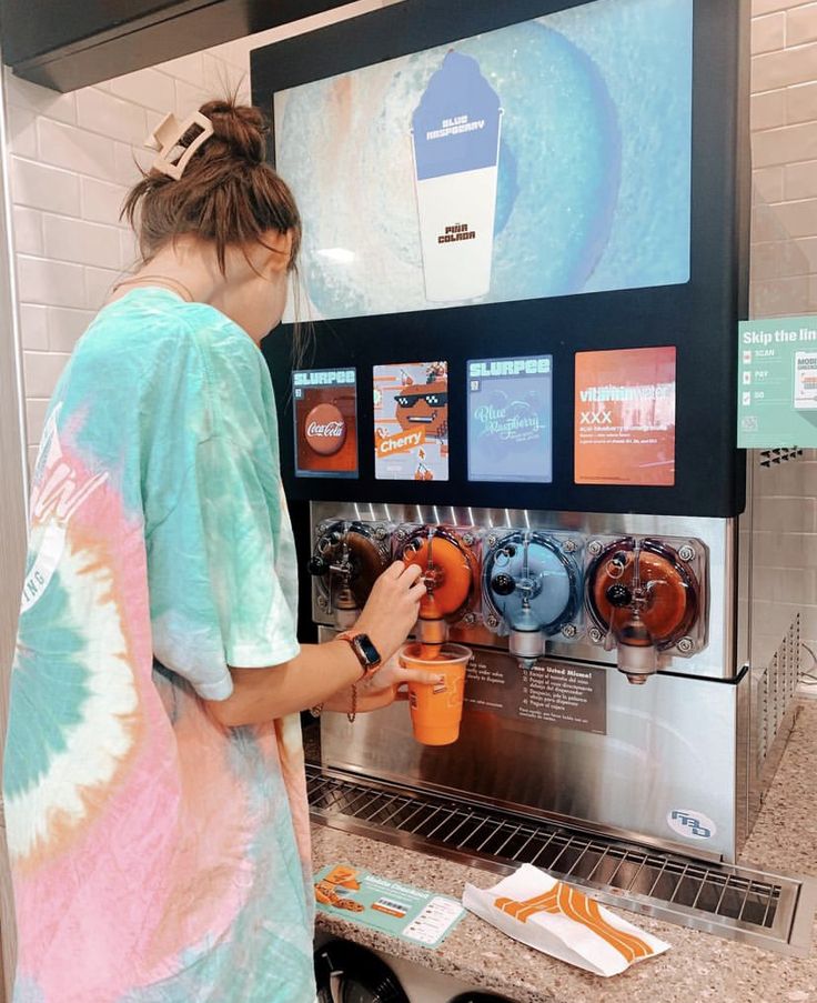 a woman standing in front of a machine filled with drinks and icecream cups