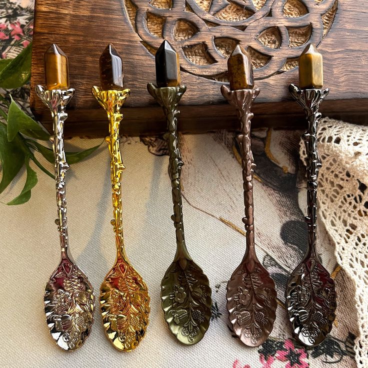 four metal spoons sitting on top of a table next to a wooden holder with flowers