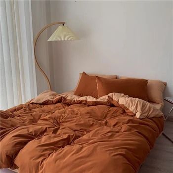 an orange comforter on a bed in a room with white walls and flooring