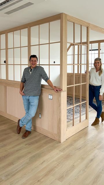 two people standing next to each other in a room with wood floors and windows on the walls