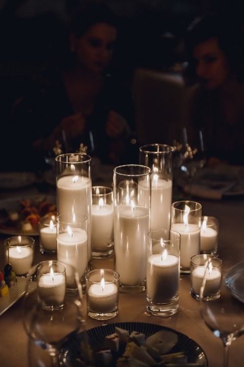 many candles are lit on a table with people in the background and plates full of food