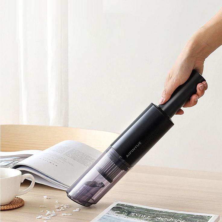 a person is using an electric vacuum cleaner on a table with books and coffee mugs