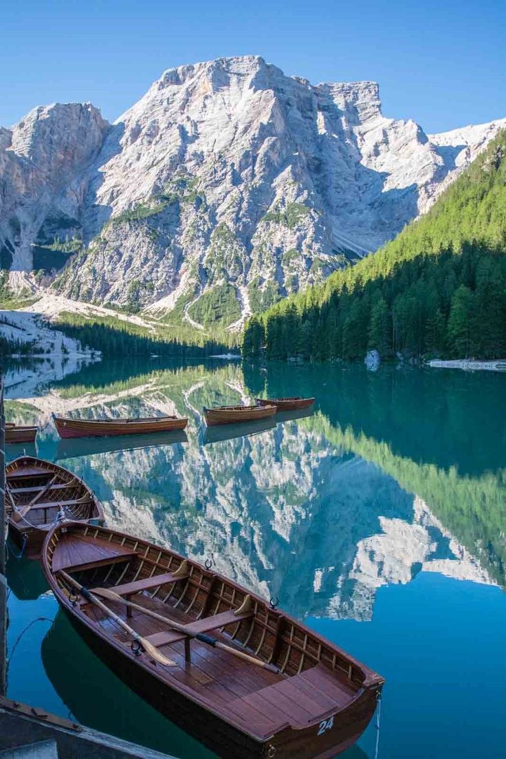 three boats are docked at the shore of a mountain lake