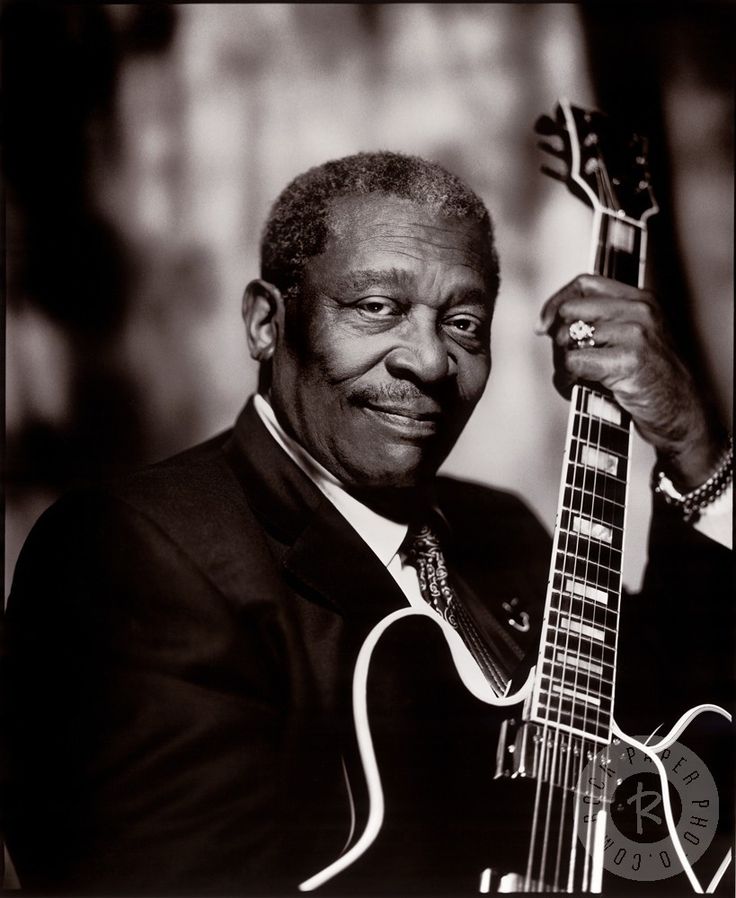 a black and white photo of a man holding a guitar in his right hand while wearing a suit