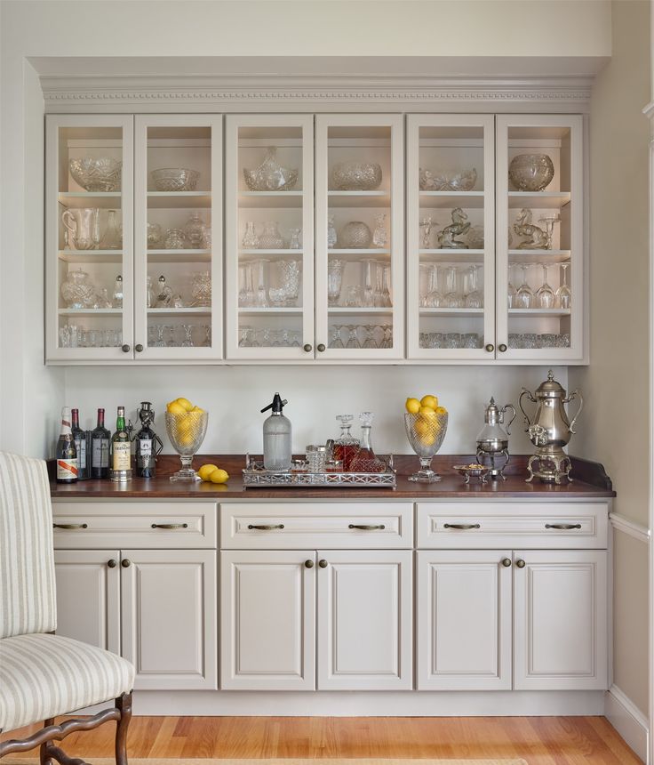 a kitchen with white cabinets and glass doors on the back wall, along with a striped chair