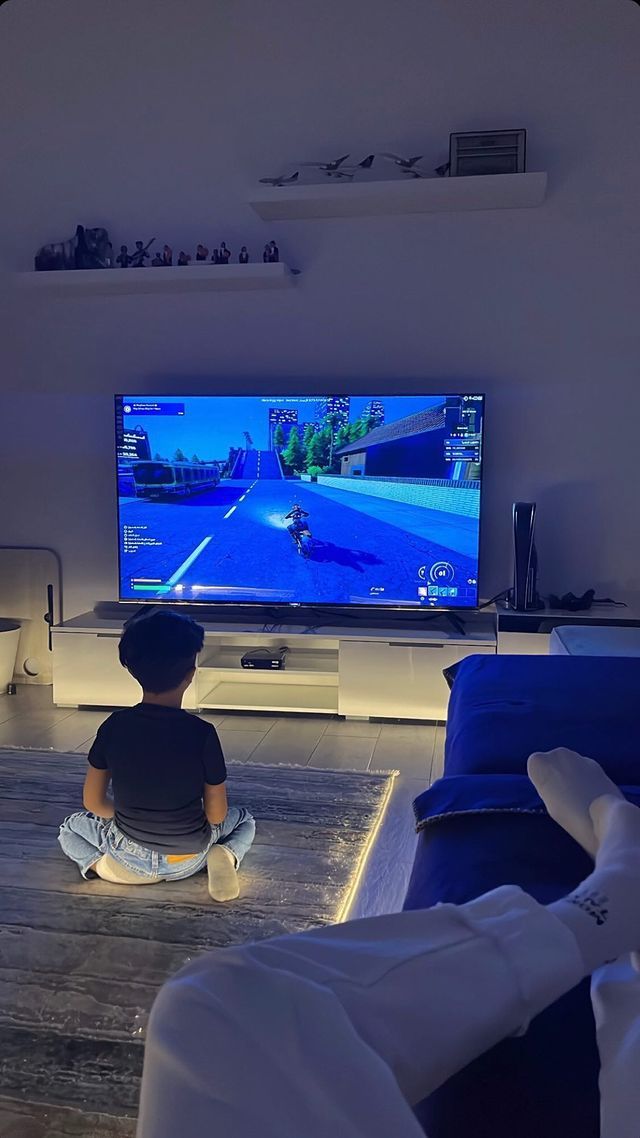 a young boy sitting on the floor in front of a tv playing video games at night