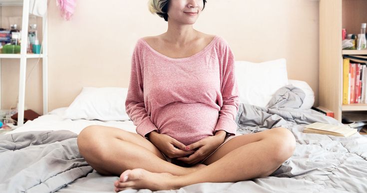 a pregnant woman is sitting on her bed