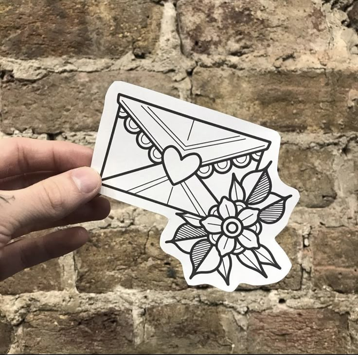 a hand holding up a sticker that has an envelope with hearts and flowers on it